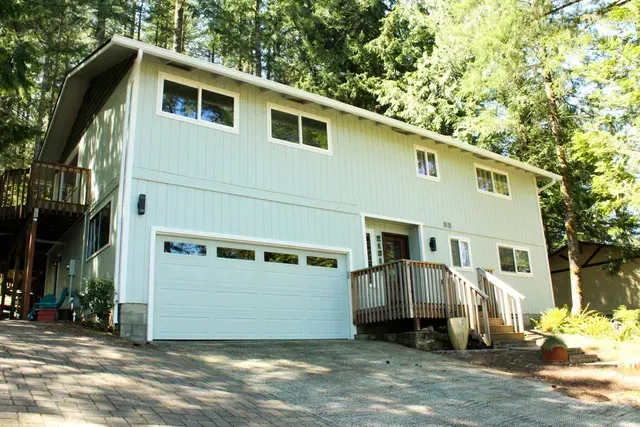 White two-story house with a garage, front deck, and trees surrounding it