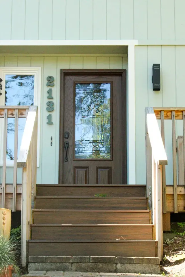 Front porch with brown wooden steps leading to a white house door with glass panel and side lights