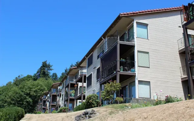 Row of beige apartment buildings on a grassy hillside under a clear blue sky