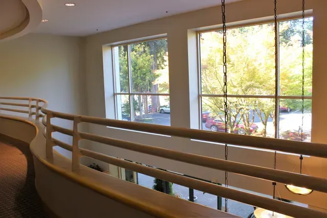 Interior hallway with wooden railings beside large windows and bright trees outside