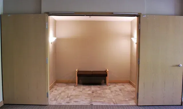 Open doorway to a small room with a bench centered against a beige wall and patterned tile floor.