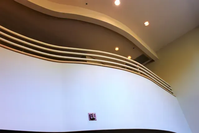 Curved white interior wall with gold trim and recessed ceiling lights above a dark baseboard
