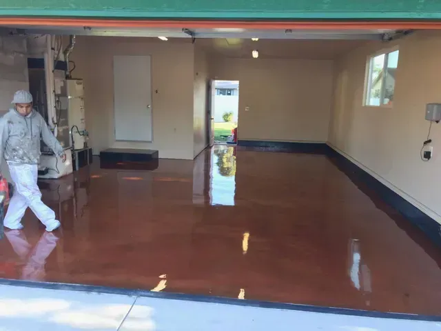 Worker mopping a glossy red floor in a large empty room with beige walls and windows