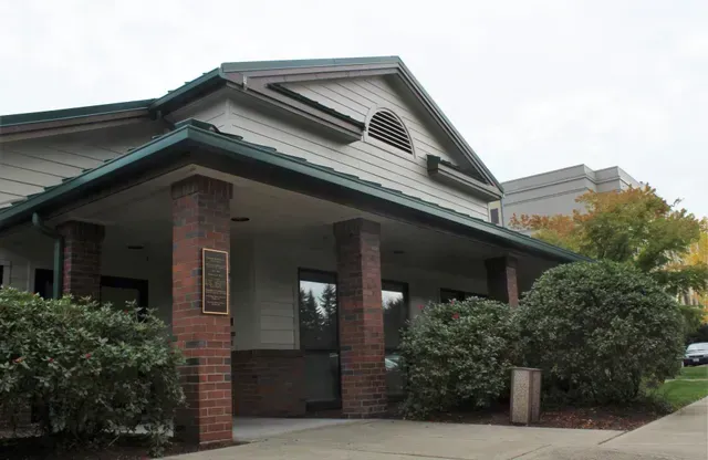 Brick building entrance with green roof, columns, and shrubs outside