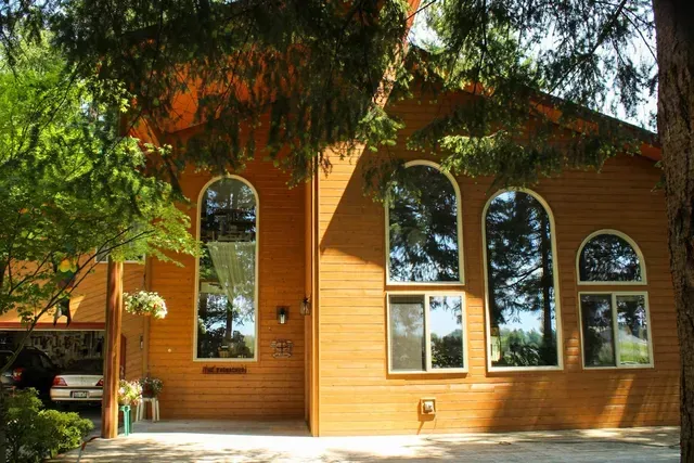 Orange wooden building with tall arched windows and trees casting shade in front