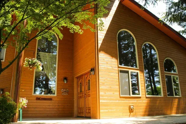 Wooden house with tall arched windows and a tree in front, lit by warm sunlight