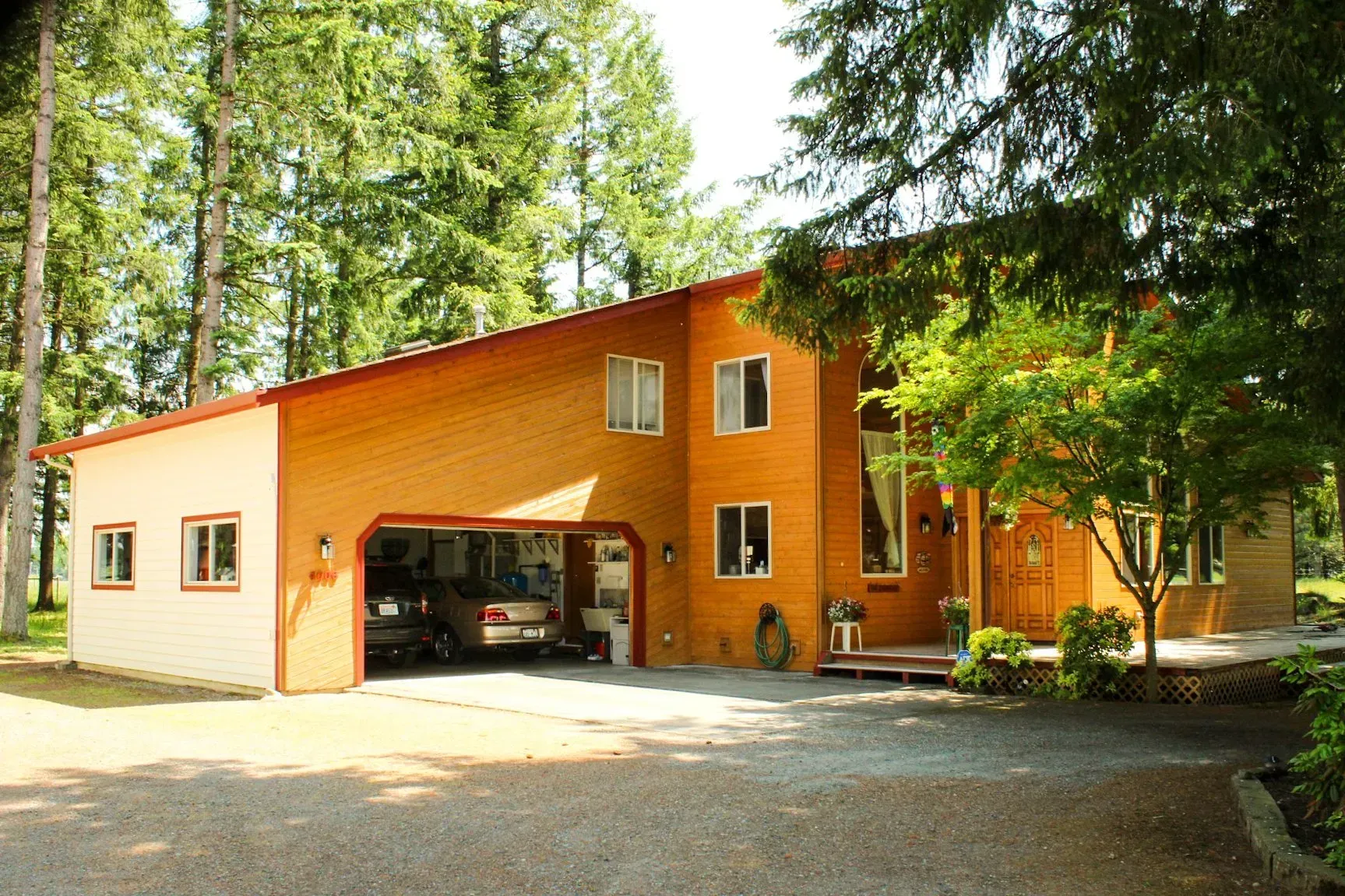 Orange house with open garage in a wooded driveway, surrounded by tall trees