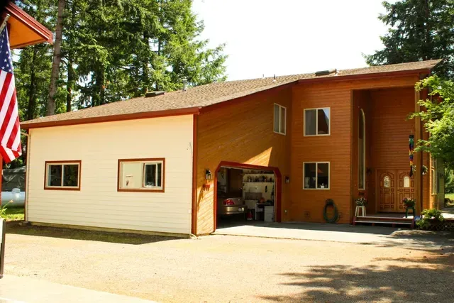 Two-tone house with open garage and American flag in a wooded setting