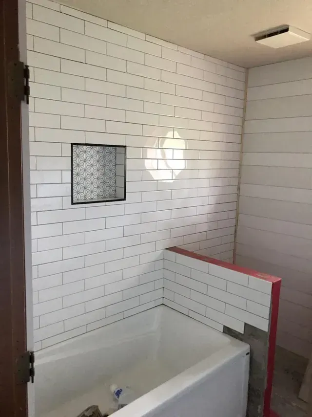Bathroom with white subway-tile wall, hanging light, and bathtub partially blocked by a red-topped half wall
