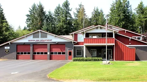 Red fire station building with garage bays, white trim, and an American flag in front
