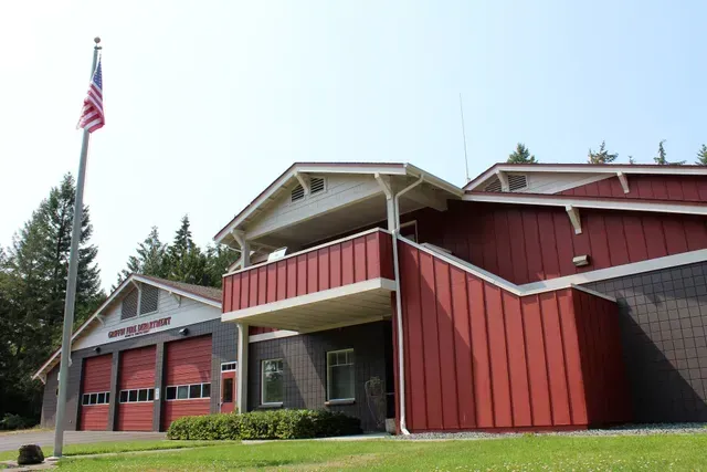 Red fire station with American flag and garage bays on a grassy lot
