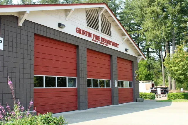 Red fire station building with three garage doors and forested surroundings