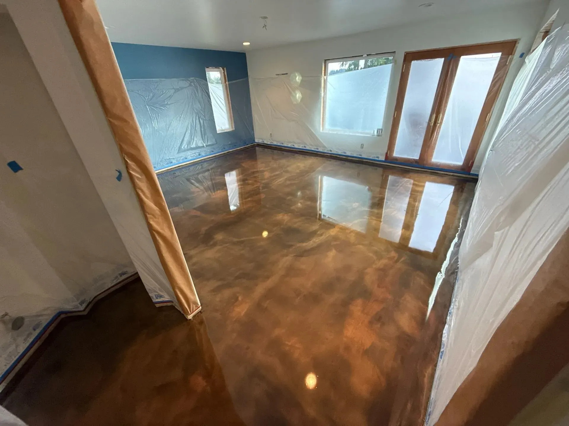 Empty modern room with glossy brown floor, blue accent wall, and large windows/door to a deck