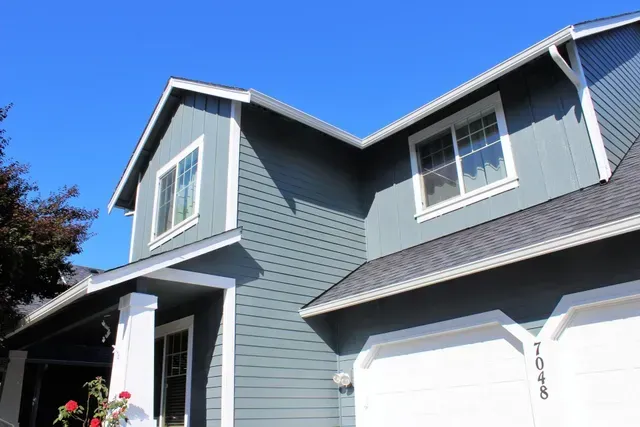 Blue-gray two-story house with white trim and a steep roof under a clear sky
