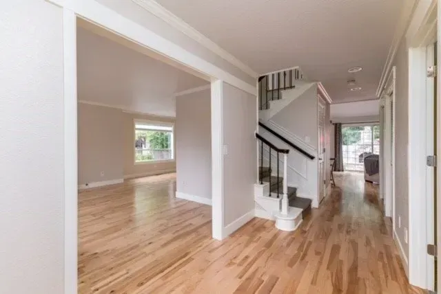 Bright empty home interior with hardwood floors, hallway, staircase, and open living space