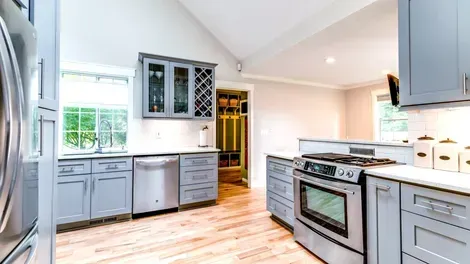 Bright modern kitchen with gray cabinets, stainless steel stove, wood floors, and large windows