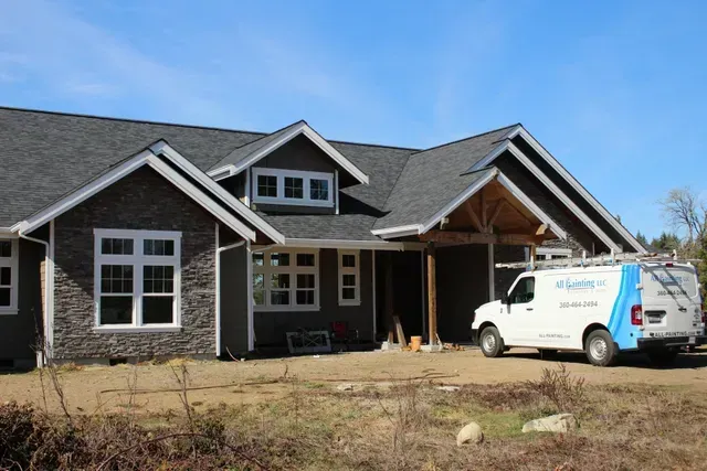 New house with dark stone siding and a white work van parked in front under construction