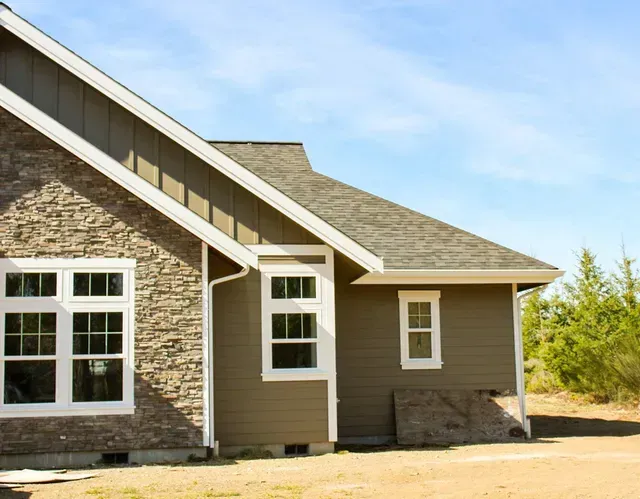 Exterior of a stone and beige house with white-trimmed windows under a blue sky