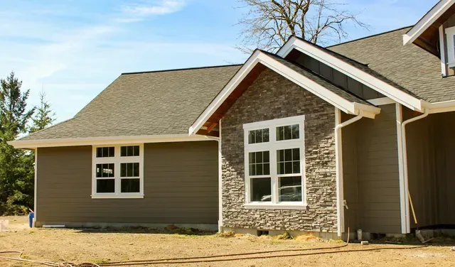 New house exterior with brown siding, stone accents, and white-trimmed windows under a blue sky