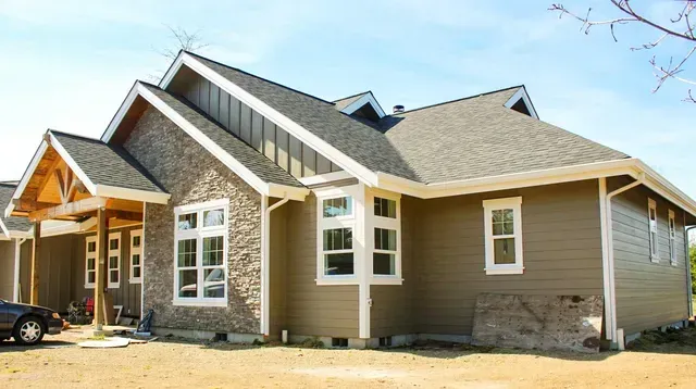 New suburban house with tan siding and stone exterior under construction on a sunny day