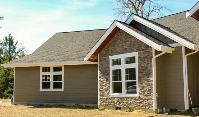 Single-story house with tan siding, stone facade, and white-trimmed windows under a gray roof