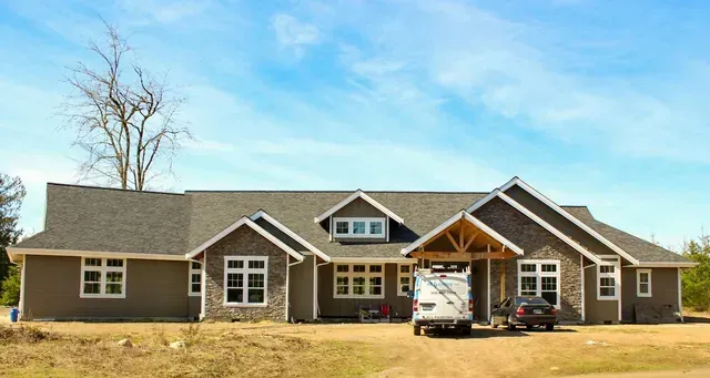 Single-story gray house with a gabled roof and a car parked in the driveway under a blue sky
