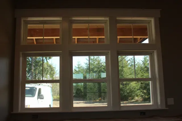 Large window with wood trim reflecting trees and a white van outside, viewed from indoors