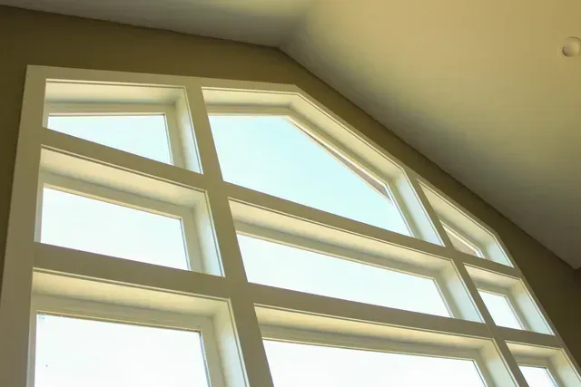 Sunlit white-framed windows with an angled upper pane and beige interior walls