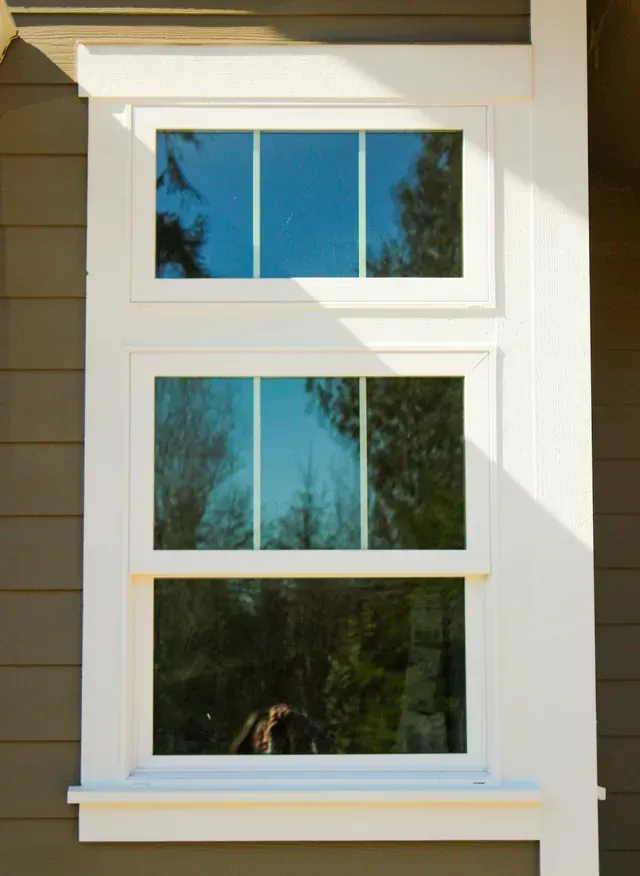 White-framed window on a beige house reflecting trees and blue sky