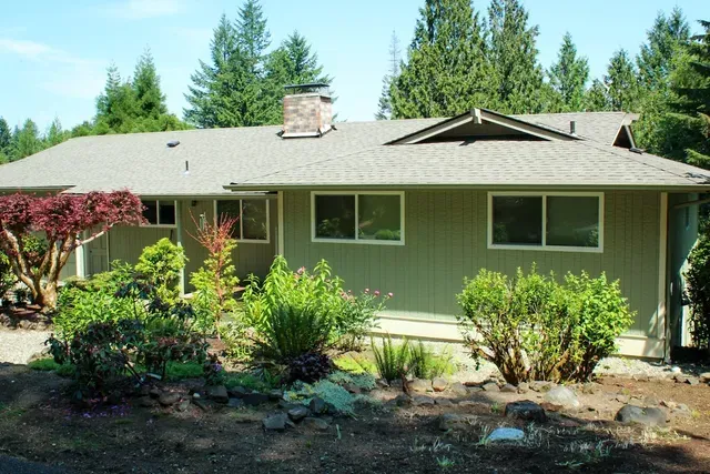 Suburban house with green roof, large windows, and landscaped front yard in daylight
