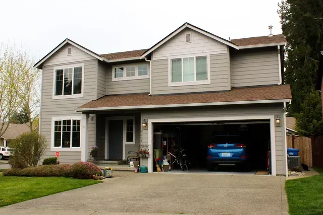 Two-story suburban house with a double garage and a blue car parked inside