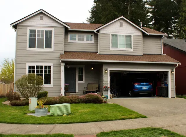 Two-story suburban house with gray siding, a front lawn, and a blue car in the open garage