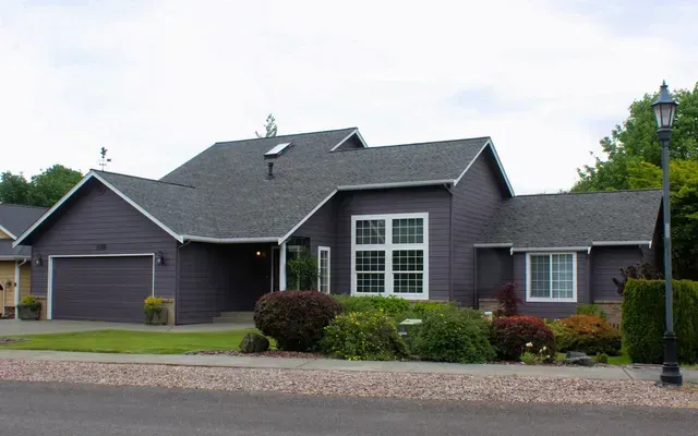 Suburban dark-gray house with a two-car garage, large front window, and landscaped yard