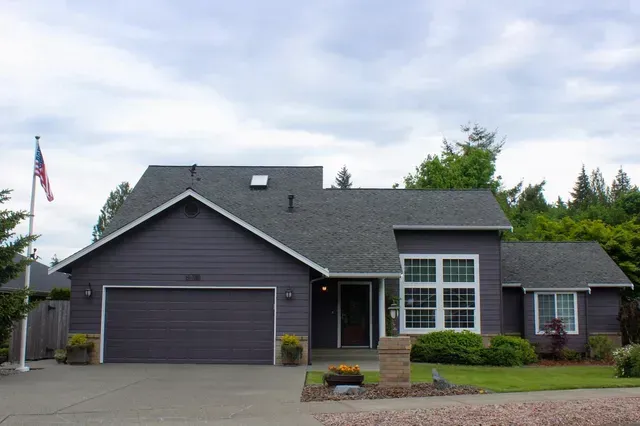 Dark gray suburban house with two-car garage, front lawn, and an American flag under cloudy sky