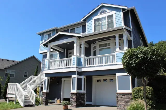Blue two-story house with white trim, front porch, and garage under a clear sky