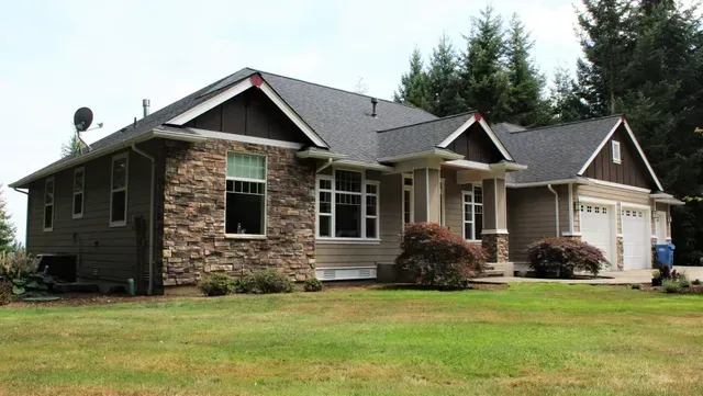Single-story suburban house with dark siding, stone accents, and a three-car garage on a grassy lot