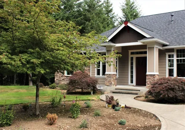 Front yard of a suburban house with a porch, curved walkway, trees, and landscaped garden.
