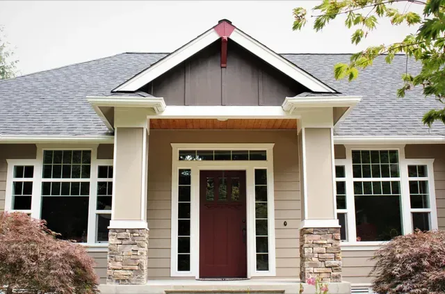 Front view of a house with beige siding, stone columns, and a dark red front door