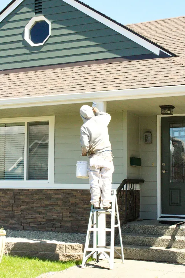 Person painting a house exterior while standing on a ladder
