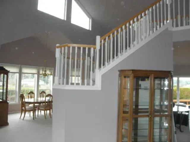 Bright foyer with white staircase, wooden railing, and dining area by large windows