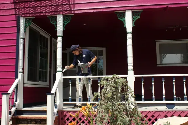 Person on a porch using a power washer beside red siding and white railings