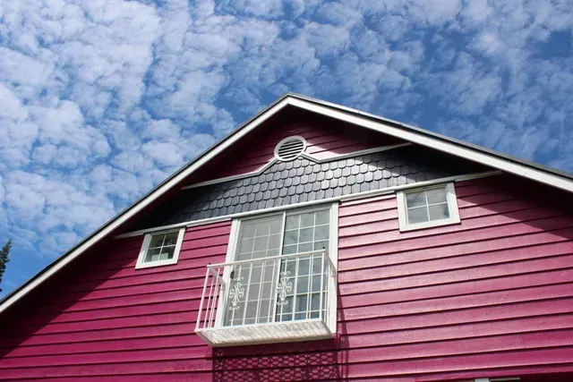 Pink house exterior with white-trimmed balcony against a cloudy blue sky