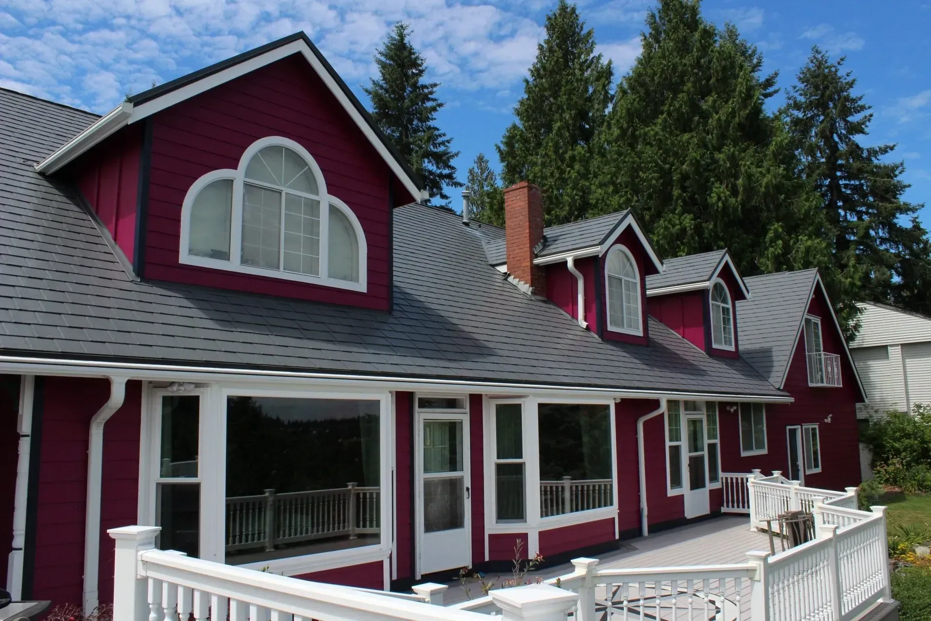 Red house with white trim and arched dormer windows, seen from the front under a blue sky.