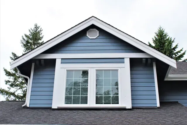Blue house gable with white trim and large front window under a dark roof