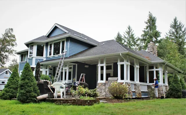 Blue two-story house with wraparound porch, white trim, and a landscaped yard