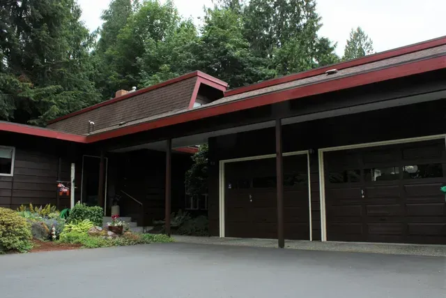 Modern house exterior with dark wood siding, red roof trim, and a covered driveway