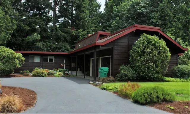 Dark wood house with red roof surrounded by trees and a curved driveway