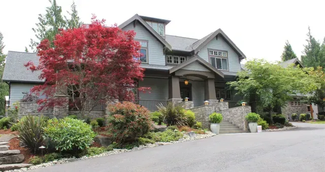 Large gray house with a red-leafed tree, landscaped garden, and driveway