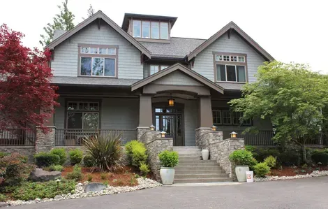 Large gray house with stone porch, front steps, and landscaped yard with red and green trees