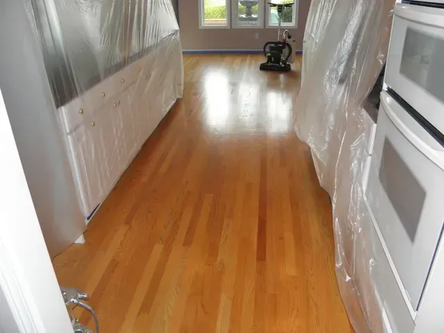 Kitchen with hardwood floor, covered cabinets, and plastic-wrapped appliances in a renovated room.